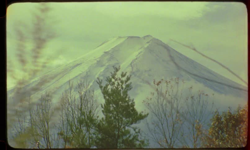 Vintage 8mm footage reveals the majestic snow-capped peak of Mount Fuji through the trees on a hazy day in Japan