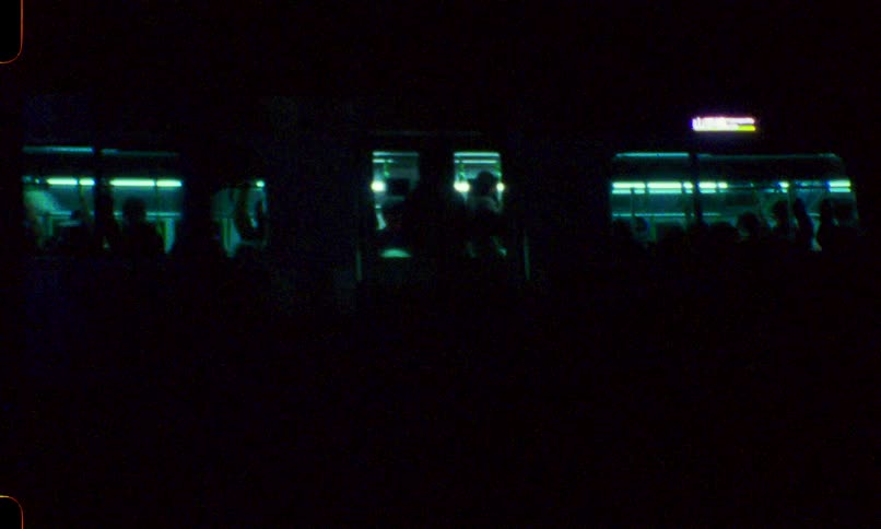Vintage film captures a passing commuter train at night, its glowing windows revealing silhouettes of passengers against the dark cityscape