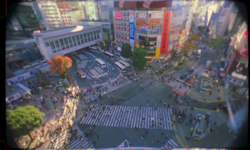 A vintage, high-angle view of the bustling Shibuya Crossing in Tokyo shows crowds of people and traffic moving through the intersection