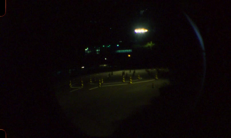 A vintage film-style shot zooms out from a driving course at night to a fisheye peephole perspective as a lone car passes