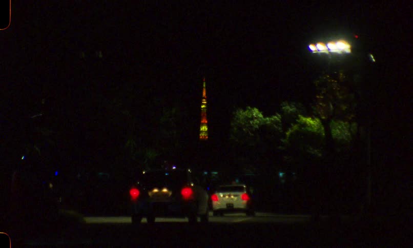 Vintage 16mm film captures cars at night with the colorful, illuminated Tokyo Tower in the distant background