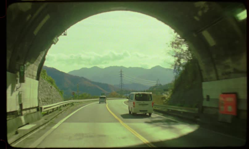 Vintage film POV shot of driving out of a dark tunnel onto a sunny highway through a mountainous landscape