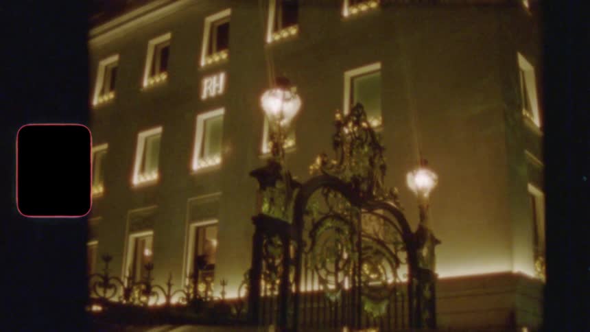 A vintage, grainy shot of an ornate, illuminated building with a grand gate at night, captured on 8mm film
