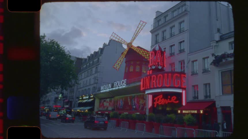 A vintage, film-style shot captures the iconic Moulin Rouge in Paris at dusk as traffic passes by on the street
