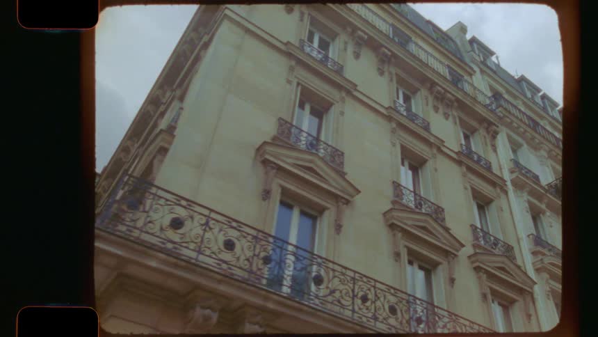 A low-angle tracking shot reveals the beautiful architecture of a traditional Parisian apartment building, captured on vintage 16mm film