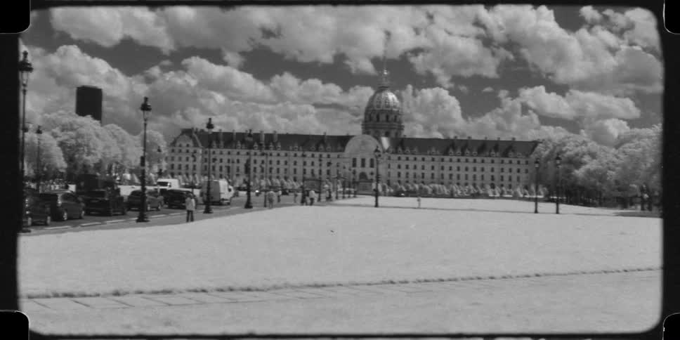 Vintage black and white 16mm infrared footage shows the iconic Les Invalides in Paris with cars driving by and people walking
