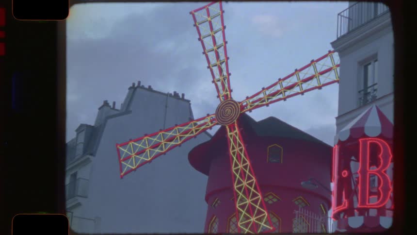 A vintage 16mm film captures the iconic neon signs and red windmill of the famous Moulin Rouge in Paris at dusk