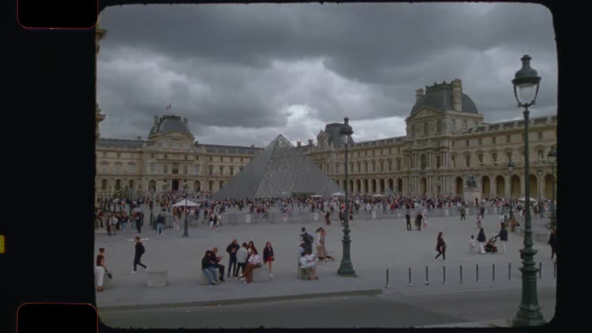 Vintage film captures a slow pan of the bustling Louvre Museum courtyard and its iconic glass pyramid on a cloudy day in Paris