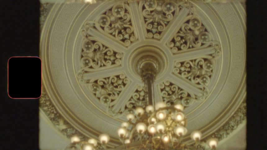 Vintage 8mm film captures the ornate details of a magnificent chandelier hanging from a decorated ceiling