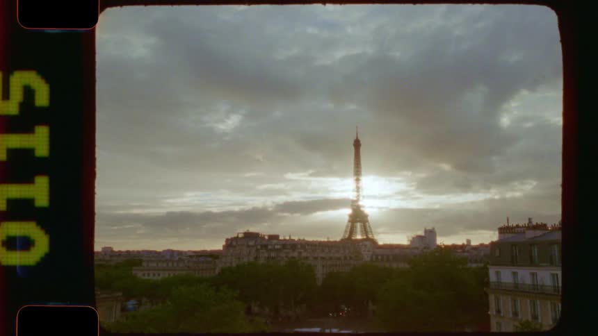 A vintage 16mm film view of the Eiffel Tower in Paris standing against a cloudy sunset sky