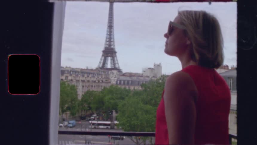 A woman in a red dress puts on sunglasses and admires the view of the Eiffel Tower from her Paris balcony in this vintage-style 8mm film clip