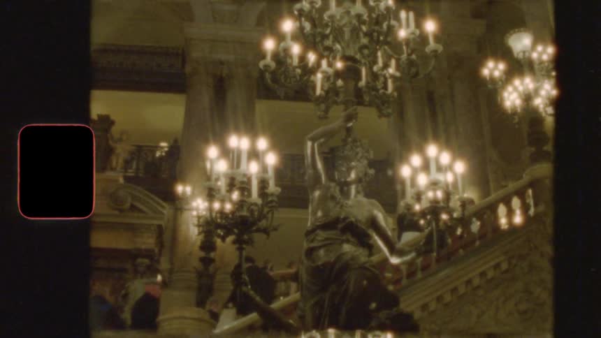 Vintage 8mm footage reveals the grand, opulent interior of a historic opera house with glowing chandeliers and statues