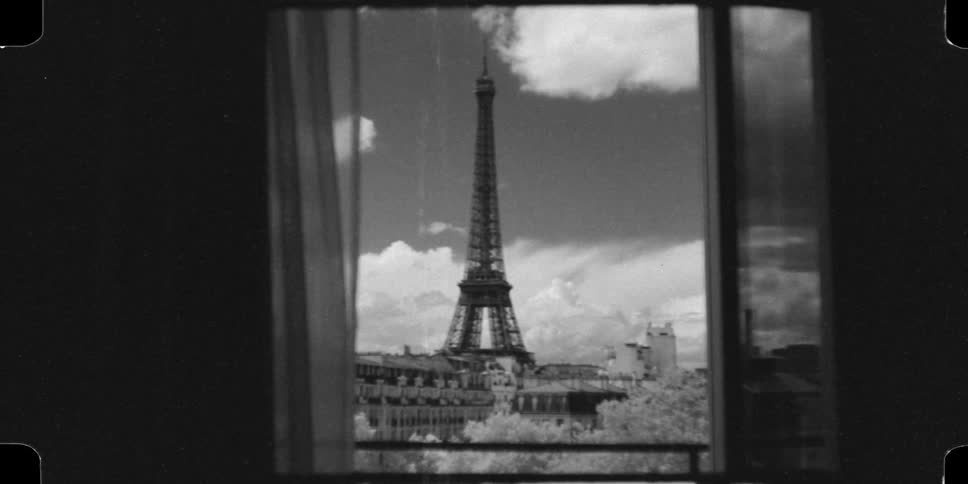 A vintage black and white 16mm film shot slowly zooms in from an apartment window to reveal the iconic Eiffel Tower in Paris
