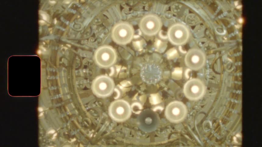 A vintage film shot looking up at a massive, ornate golden chandelier illuminating a grand hall