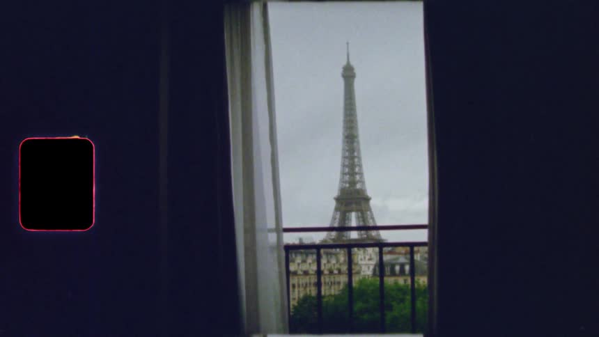 A romantic vintage film view of the Eiffel Tower seen through an apartment balcony door in Paris, France