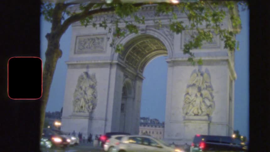 Vintage film shot captures the Arc de Triomphe in Paris as dusk settles and traffic flows by