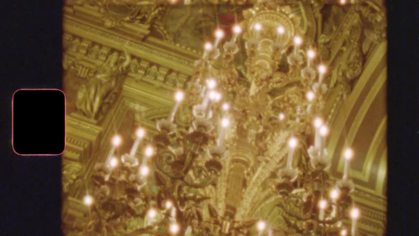 Vintage 8mm film footage shows an ornate, golden chandelier glowing in a grand, opulent hall