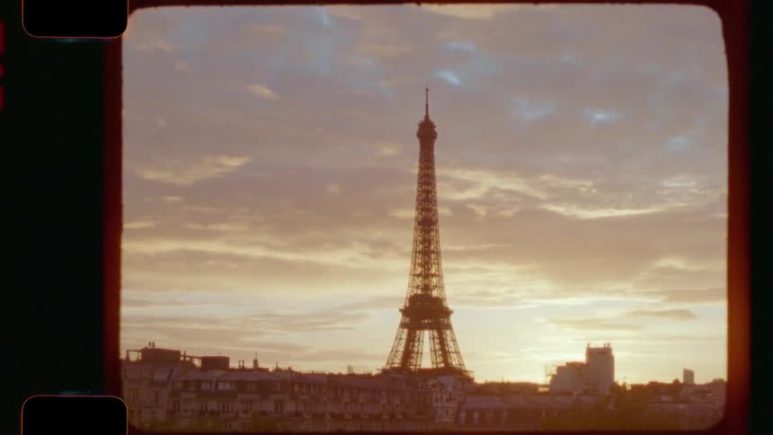 A vintage 16mm film captures the iconic Eiffel Tower silhouetted against a golden sunset sky over the Paris cityscape