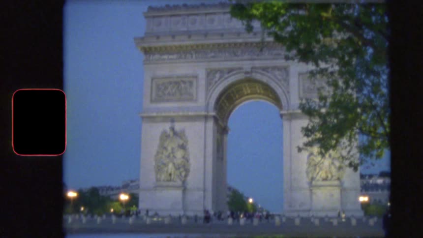 Vintage Super 8 film captures the iconic Arc de Triomphe in Paris as evening falls and traffic flows around the monument