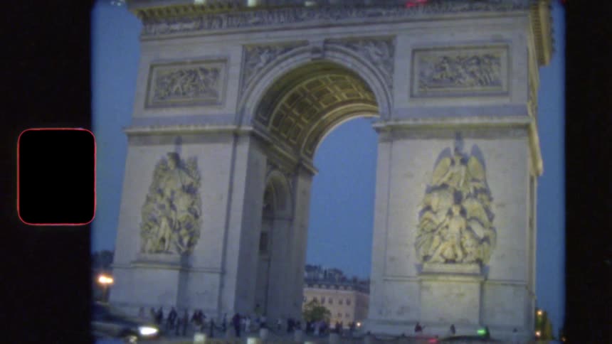 Vintage Super 8 film captures cars driving around the illuminated Arc de Triomphe in Paris at dusk
