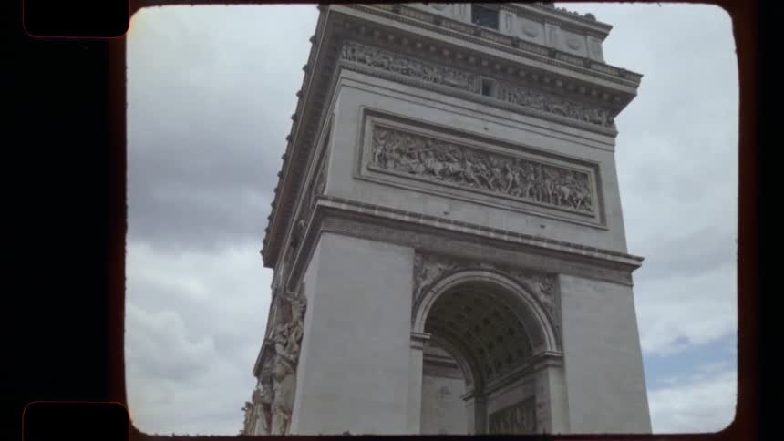 A vintage 16mm film captures a slow tilt up of the Arc de Triomphe in Paris as tourists gather below