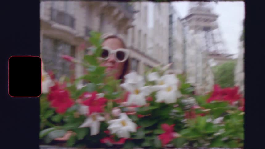 Vintage film footage shows a stylish woman smelling flowers in a Parisian flower box with the Eiffel Tower visible down the street
