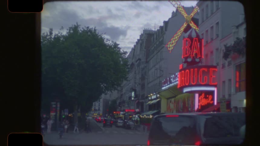 Vintage 16mm film footage of the iconic Moulin Rouge in Paris at dusk with glowing neon lights and street traffic