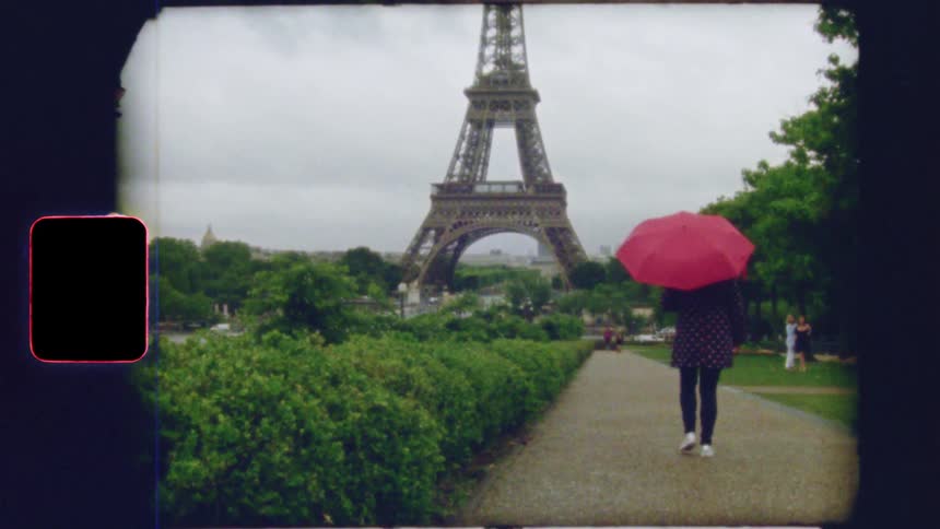 Vintage 8mm film captures a nostalgic scene of a person with a red umbrella walking towards the Eiffel Tower in Paris on a cloudy day