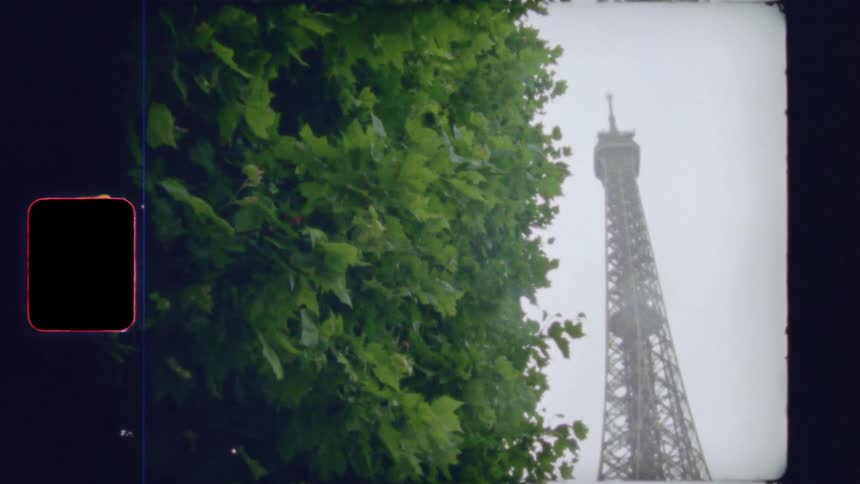 A vintage Super 8 film captures a slow tilt up the iconic Eiffel Tower from a park pathway on an overcast day in Paris