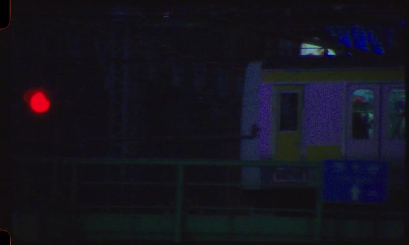 Gritty vintage film captures a blurry, dream-like view of a train passing through a neon-lit city at night