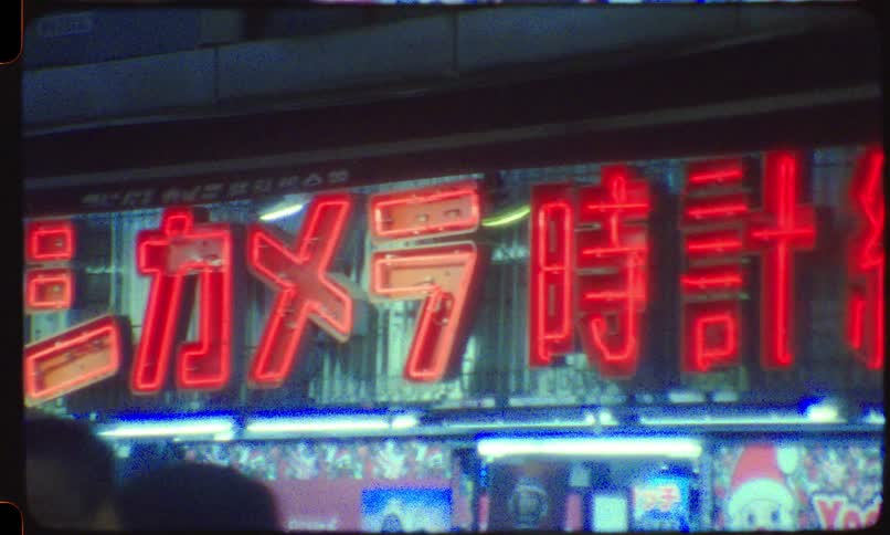 A close-up pan of a red neon sign with Japanese characters glowing at night, captured on grainy vintage film