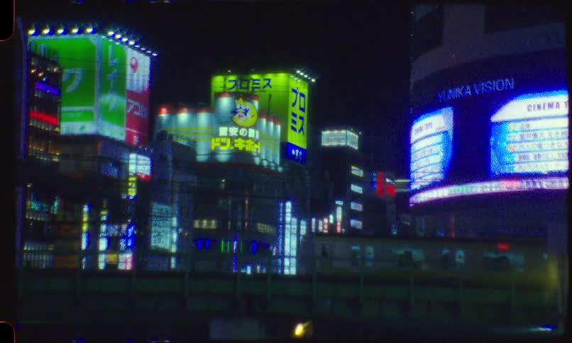 A train passes in front of the neon-lit cityscape of Shinjuku, Tokyo at night in a vintage 8mm film style