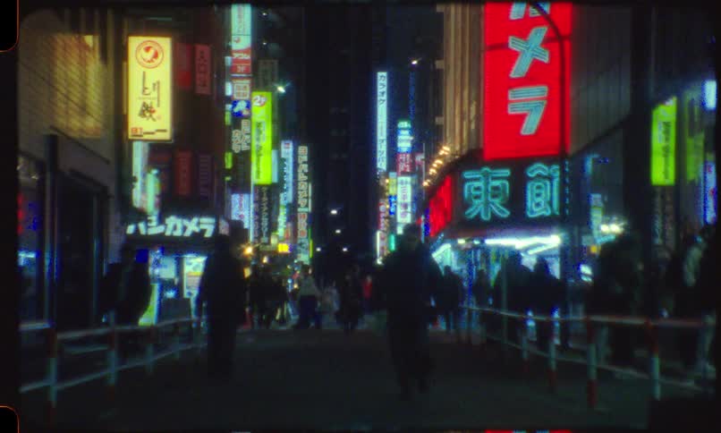 Authentic Super 8 film captures the vibrant energy of a bustling Tokyo street at night, illuminated by colorful, glowing neon signs