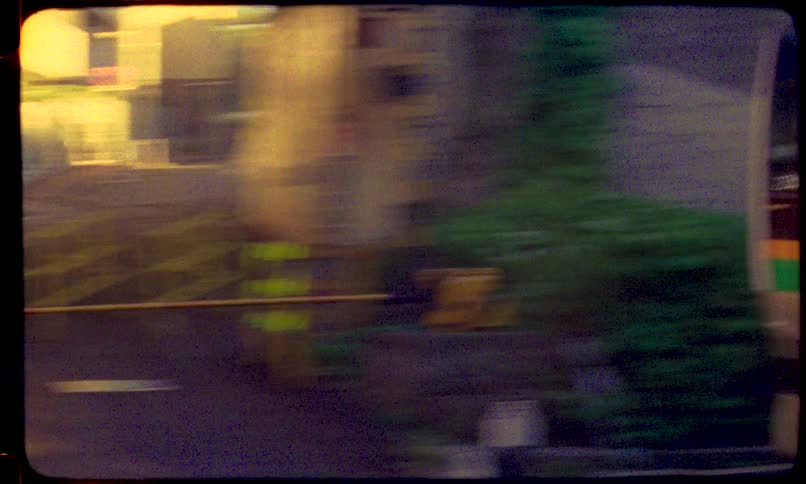 A vintage 8mm film captures a Japanese passenger train passing by and traveling down the tracks in a bustling urban city