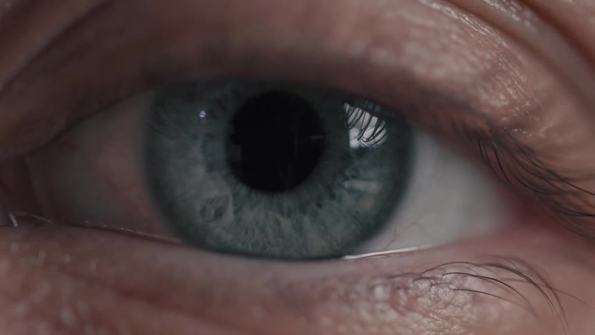 An extreme close-up shot of a human blue eye opening slowly and looking directly forward