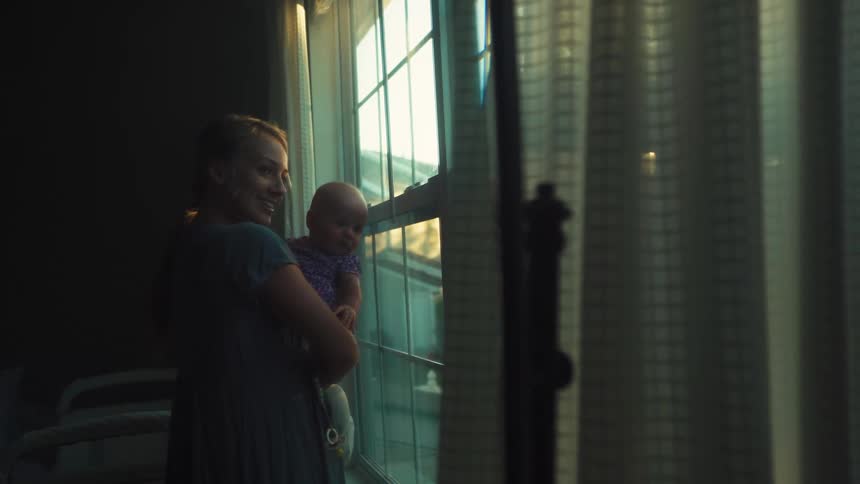 A mother and her baby share a quiet moment by the window as sunlight streams into the room
