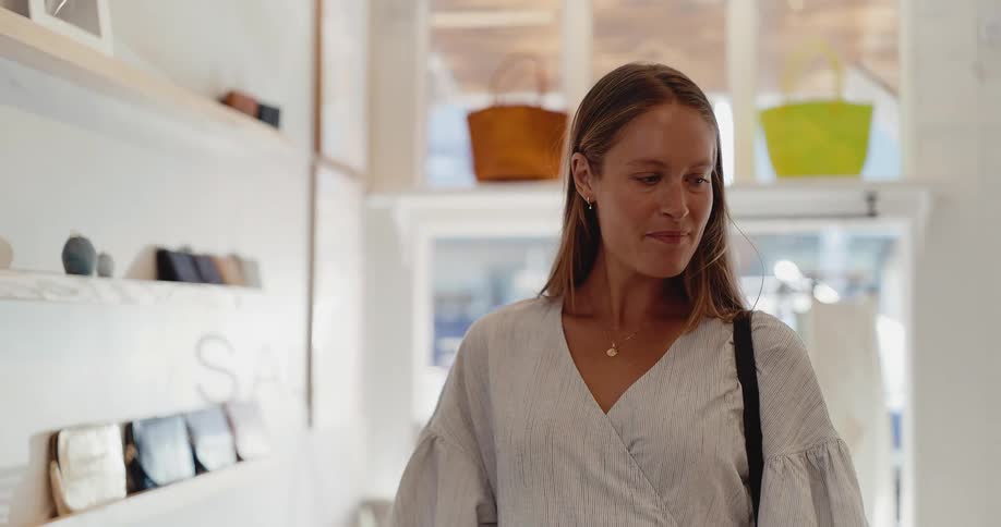 A stylish woman smiles as she happily browses in a modern, bright boutique in slow motion