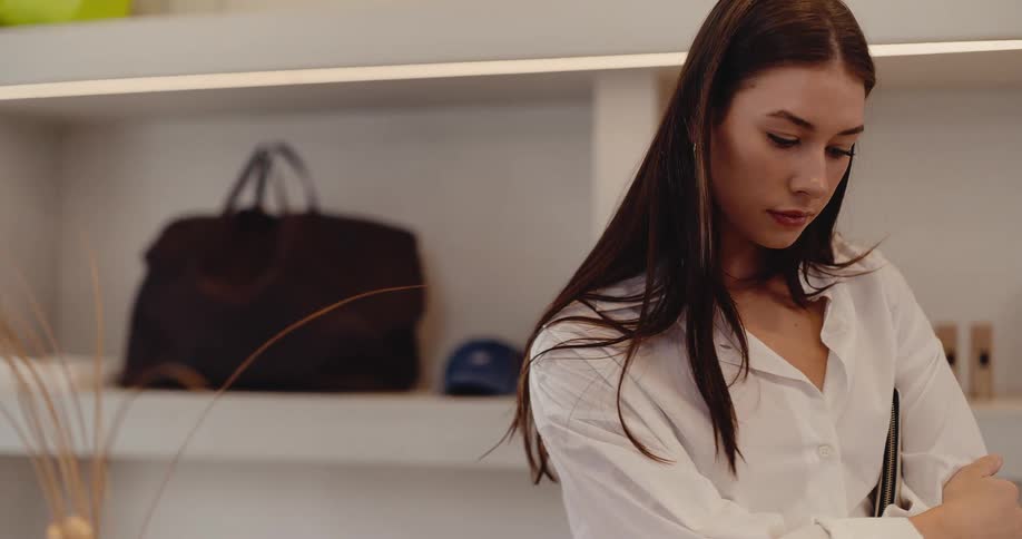 A beautiful woman with long dark hair stands thoughtfully inside a trendy, minimalist boutique