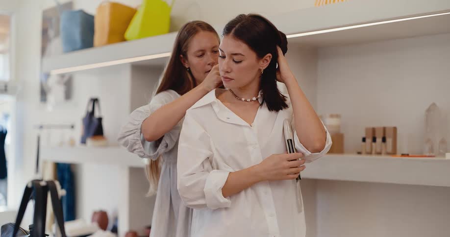 A female shopkeeper helps a customer try on a pearl necklace in a modern and minimalist boutique