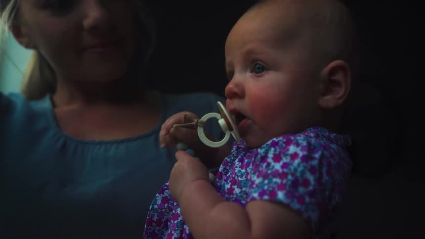 A tender moment as a mother holds her calm baby with a pacifier, illuminated by soft natural light