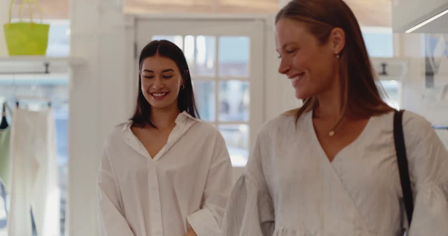Two happy female friends enjoy shopping together in a bright and airy clothing boutique in slow motion