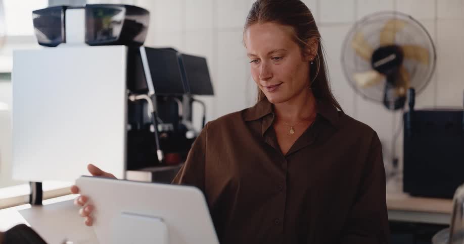 Friendly female barista takes a customer's order using a modern POS system in a bright coffee shop