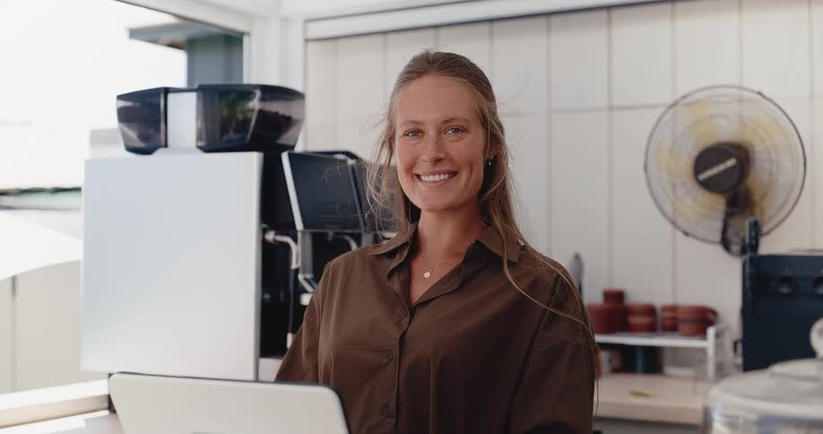 Portrait of a smiling young female barista standing behind the counter in her modern coffee shop