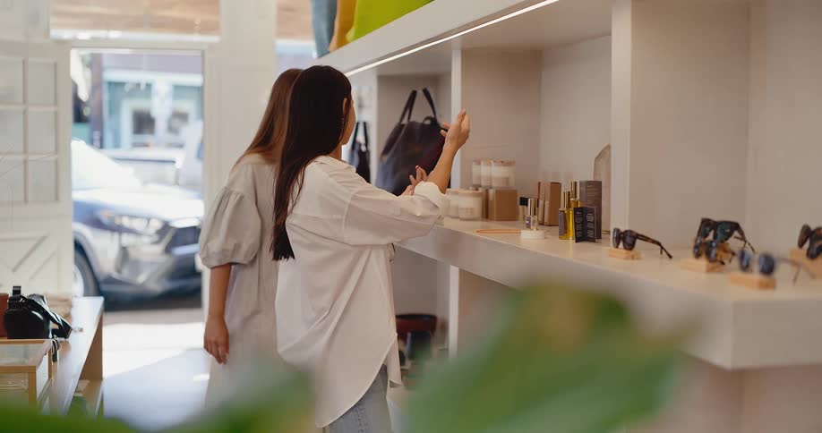Two young women shop together, looking at a delicate necklace in a bright, modern boutique