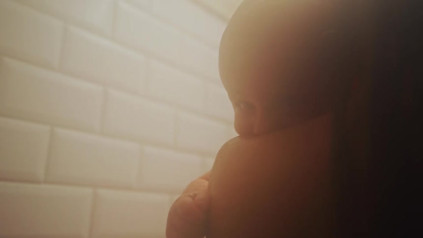 A tender close-up shot shows a newborn baby resting securely on its parent's shoulder