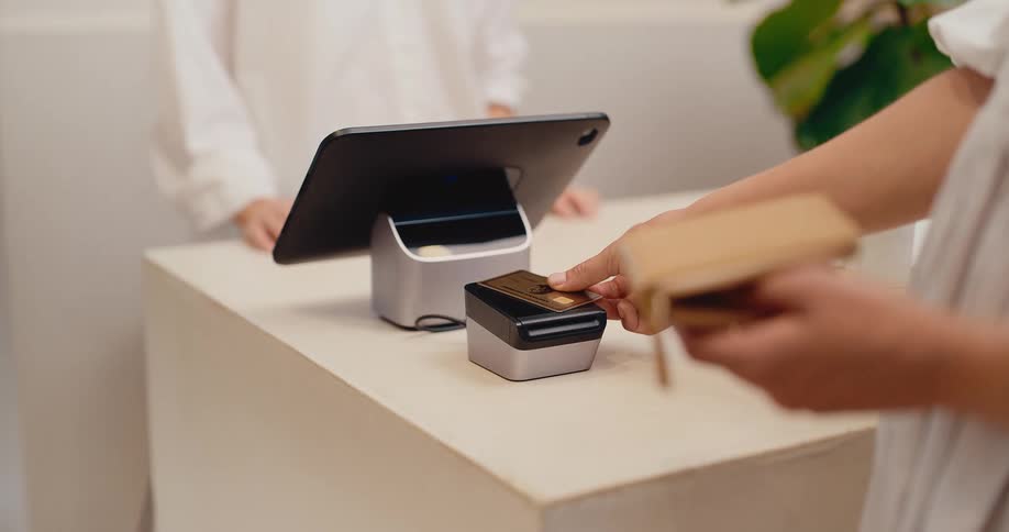 A customer completes a purchase in a retail store by tapping their credit card on a modern contactless payment terminal
