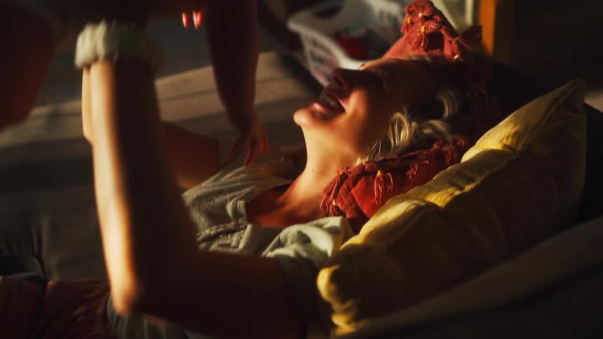 A mother joyfully lifts her baby up while they play together on the couch, bathed in warm sunlight