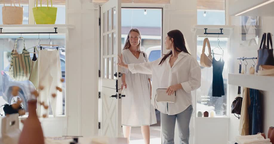 Two stylish young women enter a bright and sunny clothing boutique to go shopping in slow motion