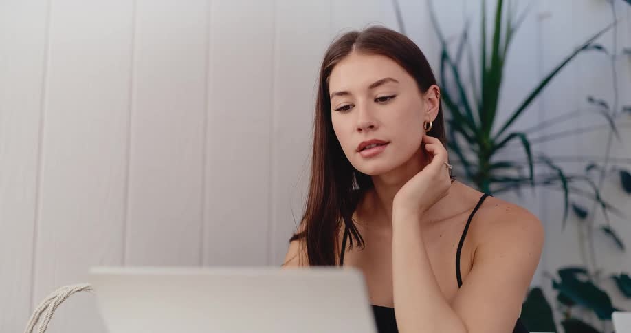 Close-up of a smiling young woman using her laptop, whose mood shifts to become thoughtful and serious