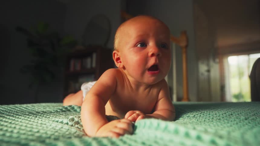 A curious newborn baby boy with blue eyes lies on his stomach on a green blanket during tummy time